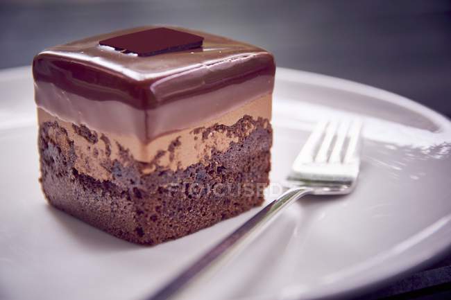 Close-up vista de chocolate Petit quatro bolo com garfo na placa — Fotografia de Stock