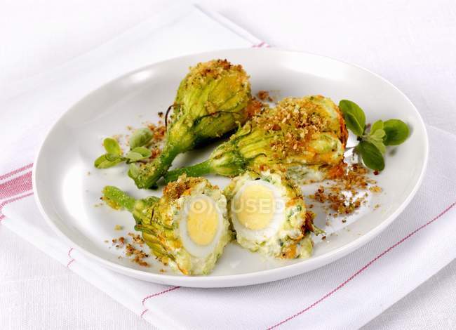 Fiori di zucchina gratinati riempiti con uova su piatto bianco — Foto stock