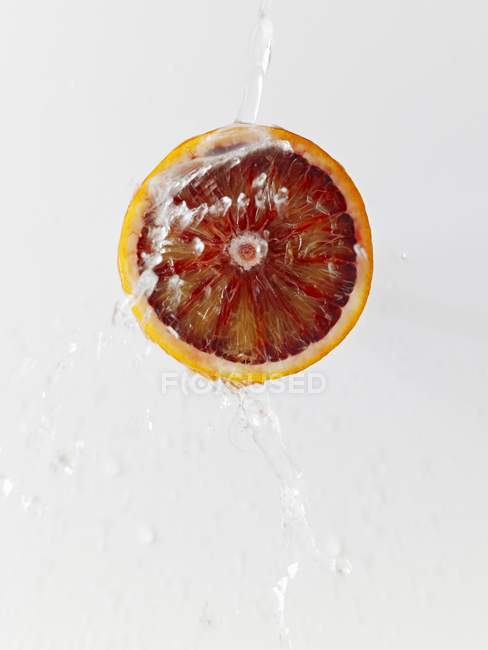 Mitad de naranja sangre con chorro de agua - foto de stock