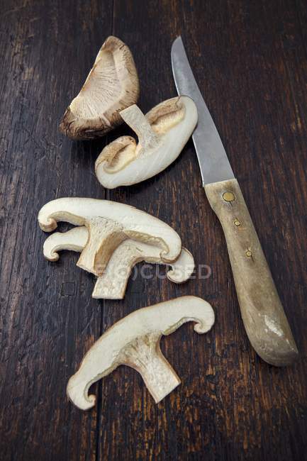 Vista close-up de um cogumelo Shiitake fatiado com uma faca em uma superfície de madeira — Fotografia de Stock
