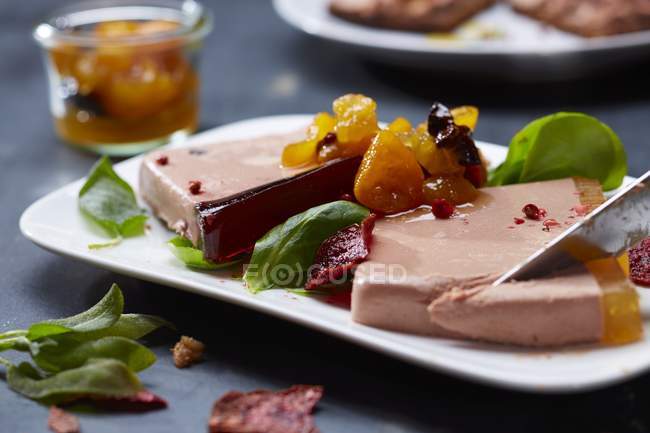 Vue rapprochée de tranches pâteuses de foie avec des feuilles et des fruits conservés — Photo de stock