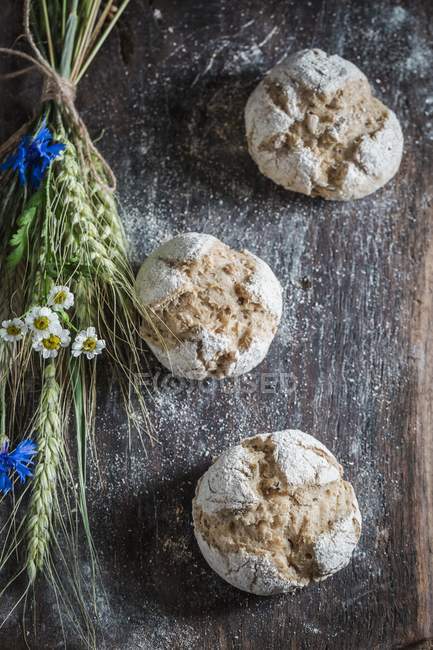 Pães integrais saudáveis com orelhas de aveia e flores em uma tábua de madeira — Fotografia de Stock