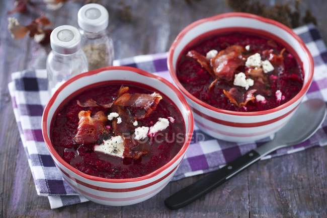 Cream of beetroot soup in white and red bowls over towel with spoon — Stock Photo