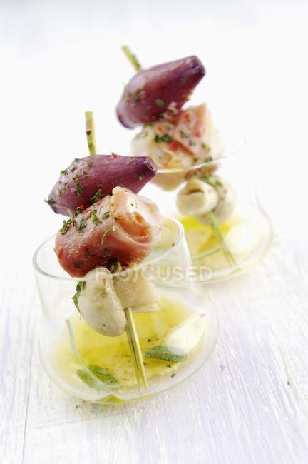 Fish kebabs with mushrooms and shallots in glasses over wooden surface — Stock Photo