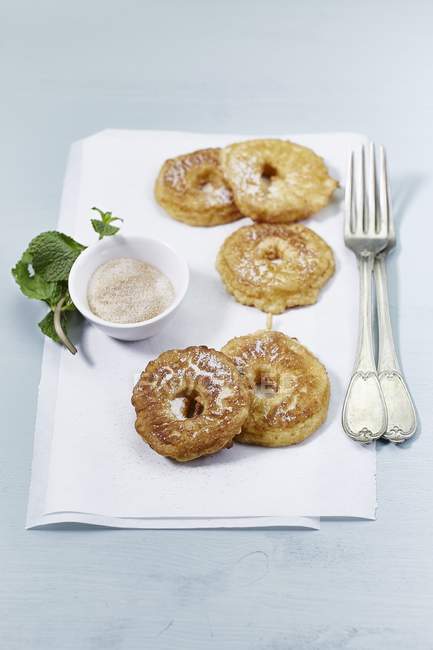 Apple rings dusted with cinnamon sugar over paper with fork and saucer — Stock Photo