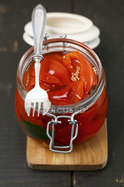 Pickled peppers in a glass jar with a fork on a chopping board — Stock Photo