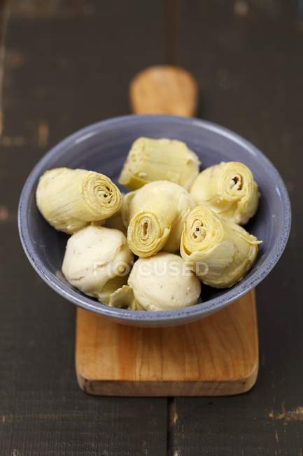 Artichoke hearts in a bowl on a chopping board with plate — Stock Photo