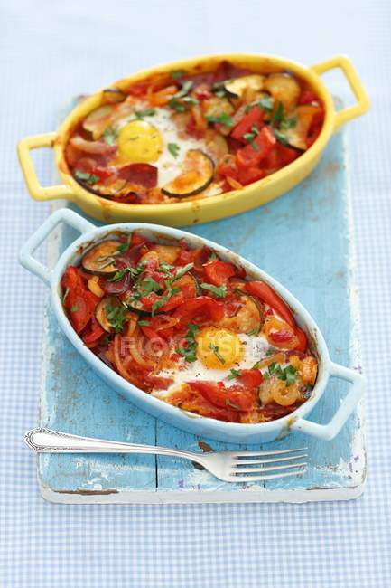Shakshuka with vegetables, egg and salami in dishes over desk with fork — Stock Photo