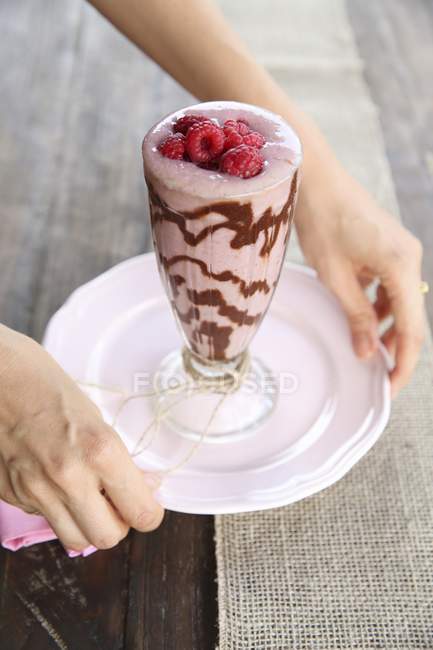 Hands holding plate with glass of smoothie — Stock Photo