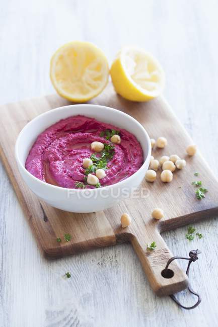 Beetroot hummus with chickpeas and lemon in white pot over wooden surface — Stock Photo