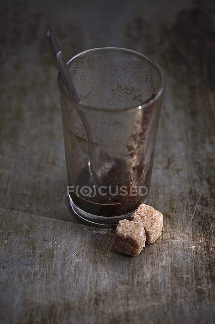 Vista de cerca de los residuos de café en un vaso con cubos de azúcar morena - foto de stock
