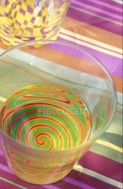 Vista de primer plano de un vaso con agua y un patrón de espiral colorido - foto de stock