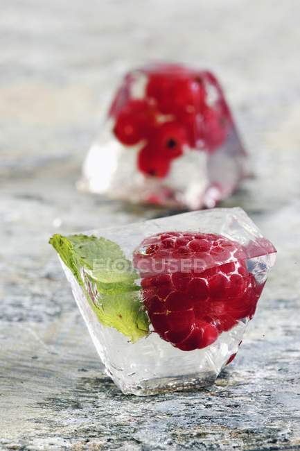 Cubo de hielo con frambuesa sobre superficie de madera - foto de stock