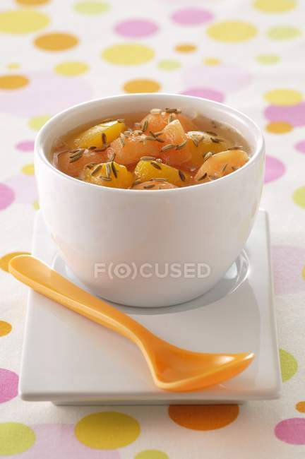 Melón guisado y melocotones con semillas de hinojo en maceta blanca sobre superficie coloreada - foto de stock