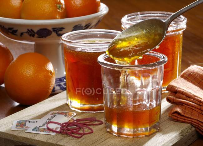 Closeup view of homemade marmalade in jars with whole oranges on the background — Stock Photo