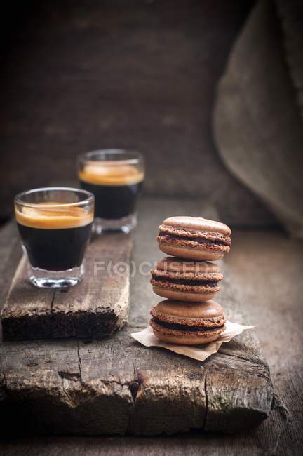 Closeup view of piled macarons with glasses of coffee on paper and wooden boards — Stock Photo