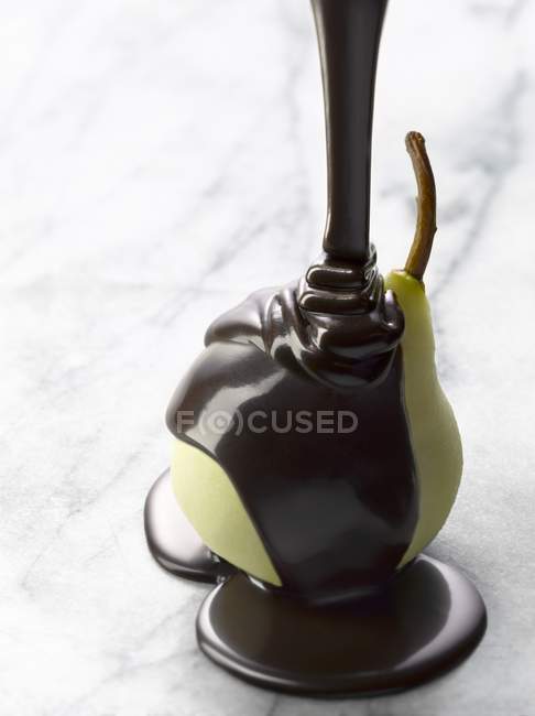 Pouring melted chocolate onto pear — Stock Photo