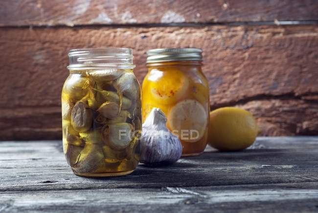 Ajo y limones conservados en tarros de albañil sobre superficie de madera - foto de stock
