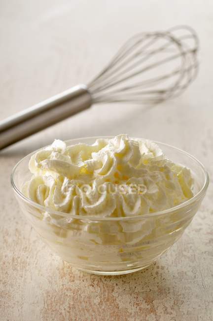 Bowl of whipped cream and a whisk over wooden surface — Stock Photo