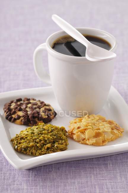 Vista de cerca del café y tres galletas crujientes con sabor diferentes - foto de stock