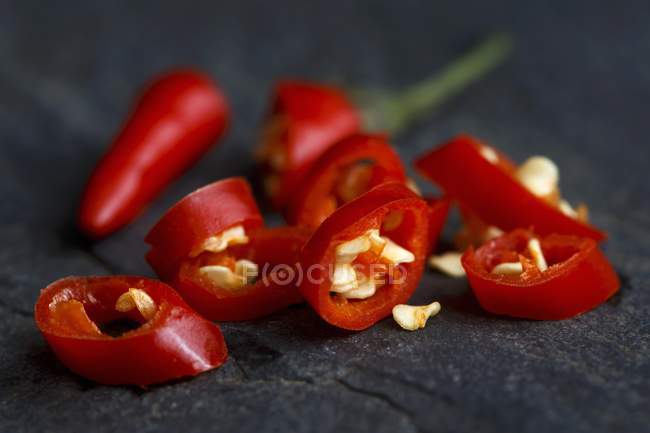 Cut fresh birds eye chilli with seeds on dark slate background — Stock Photo