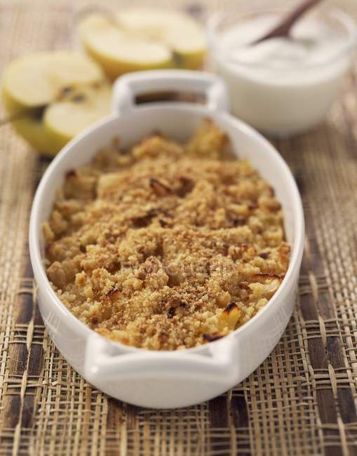 Apple crumble in white dish over straw surface — Stock Photo