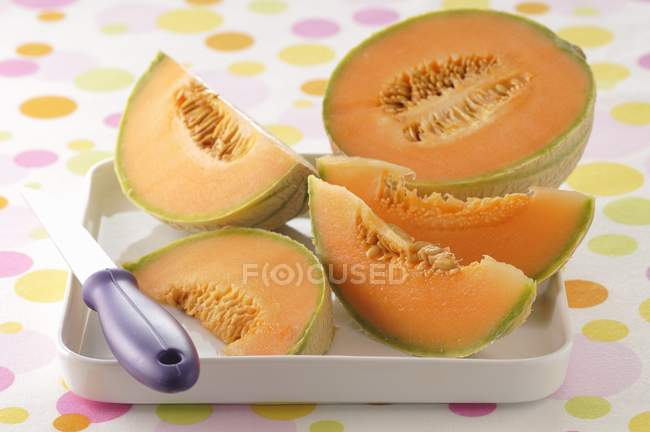 Vista de cerca del melón en rodajas con cuchillo en tazón - foto de stock