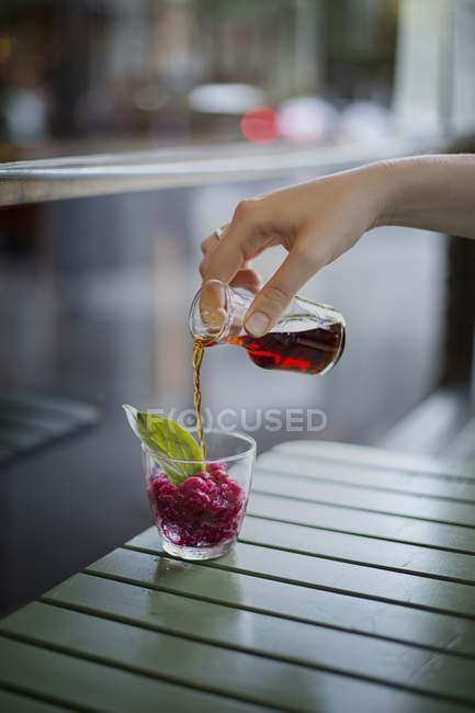 Close-up vista cortada de mão derramando licor de ervas em granita romã em um copo — Fotografia de Stock