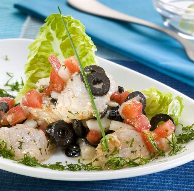 Trancher la viande avec des feuilles de salade et des légumes sur une assiette blanche sur un tissu bleu — Photo de stock