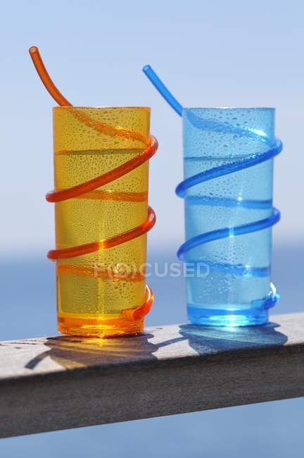 Nahaufnahme von blauen und orangefarbenen Gläsern mit Strohhalmen auf Holzplanken — Stockfoto