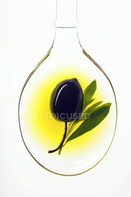Black olive in spoonful of olive oil — Stock Photo