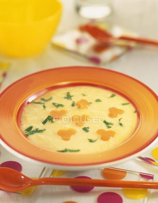 Maiscremesuppe auf orangefarbenem Teller über Tisch mit rotem Löffel — Stockfoto