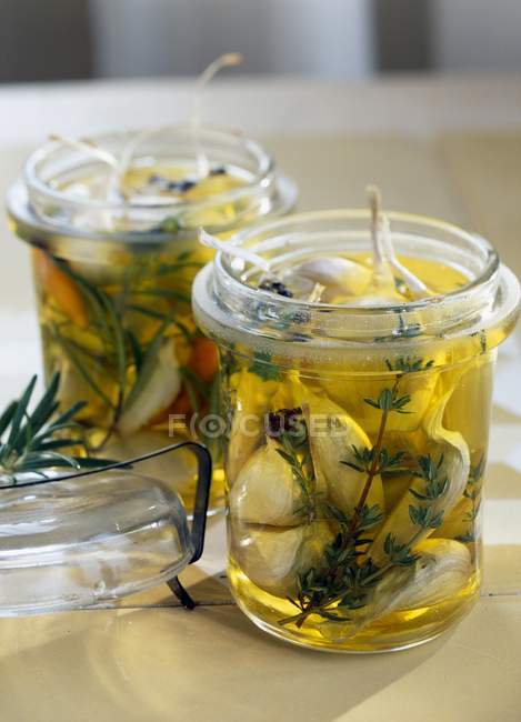Garlic marinating in oil with rosemary and thyme inglass jars over table — Stock Photo