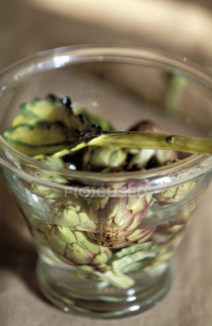 Artichokes in water at glass with spoon — Stock Photo