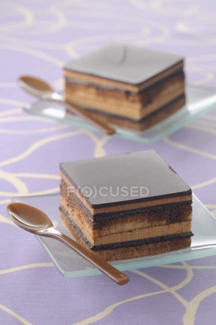 Vue rapprochée des gâteaux carrés Opra sur des assiettes avec cuillères — Photo de stock