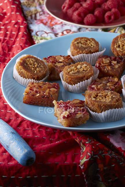 Closeup view of raspberry Namoura and Brazilian nut Burma baklava on ethnic floral tablecloth with fresh raspberries — Stock Photo