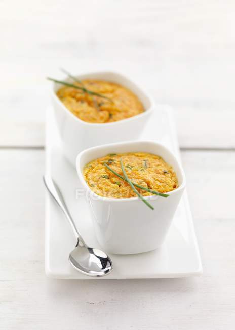 Carrot and chive Flan in small white bowls over plate — Stock Photo