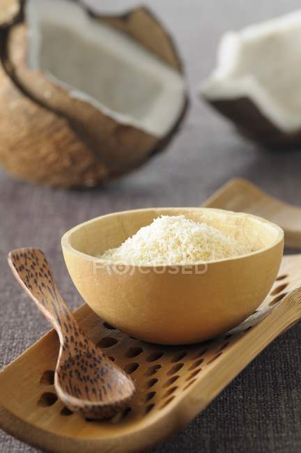 Noix de coco râpée dans un bol en bois sur un plateau avec cuillère en bois — Photo de stock