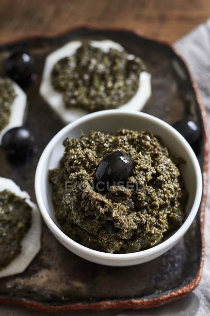 Tapenade with black olives in white pot over tray — Stock Photo