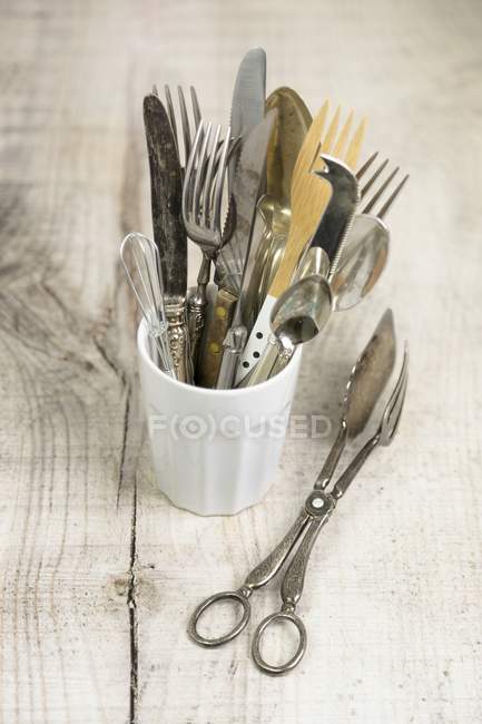 Closeup view of different cutlery and kitchen tools in white cup on wooden surface — Stock Photo