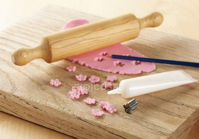 Closeup view of pink icing rolled out on a board with rolling pin, metal flower shaped cutter and white icing tube — Stock Photo