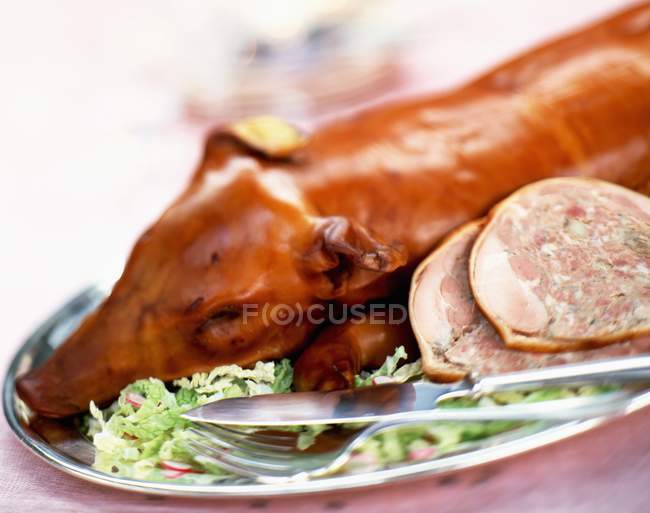 Closeup view of a stuffed suckling pig with herbs and cutlery on a tray — Stock Photo