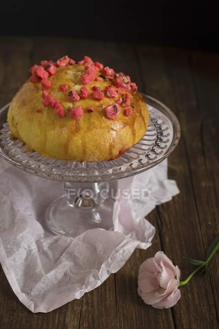 Closeup view of Brioche with dried strawberries on glass cake stand and paper on wooden surface — Stock Photo