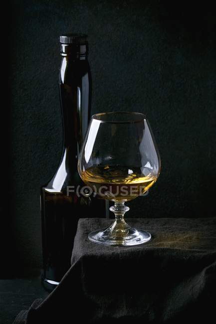 Vista ravvicinata di bottiglia e bicchiere di mela francese Calvados sulla tovaglia nera — Foto stock