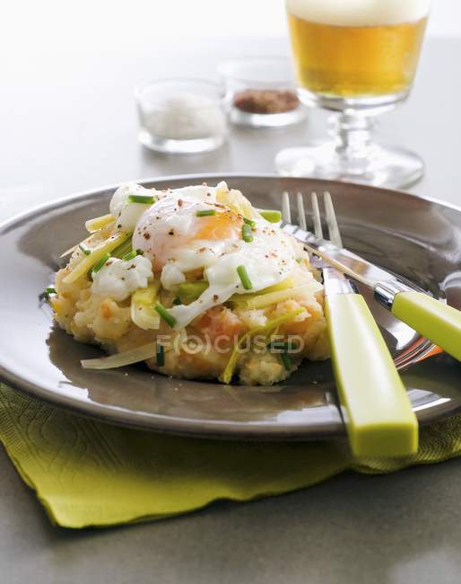 Stoemp увенчанный яйцом на коричневой тарелке с вилкой и ножом — стоковое фото