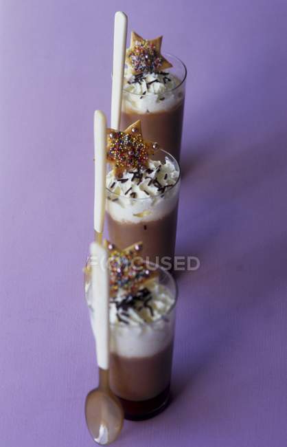 Vista de primer plano de la crema de chocolate con crema batida en vasos con cucharas y galletas en forma de estrella - foto de stock