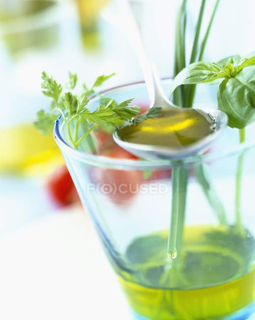 Glass of olive oil with fresh herbs and spoon — Stock Photo