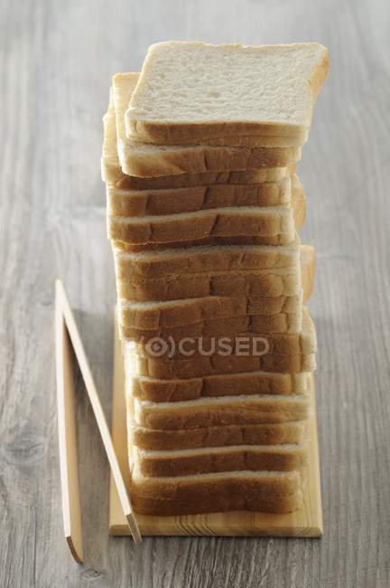 Closeup view of piled slices of bread with tongs — Stock Photo