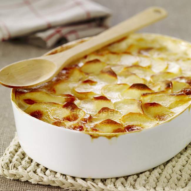 Gratin dauphinois in white dish with wooden spoon — Stock Photo