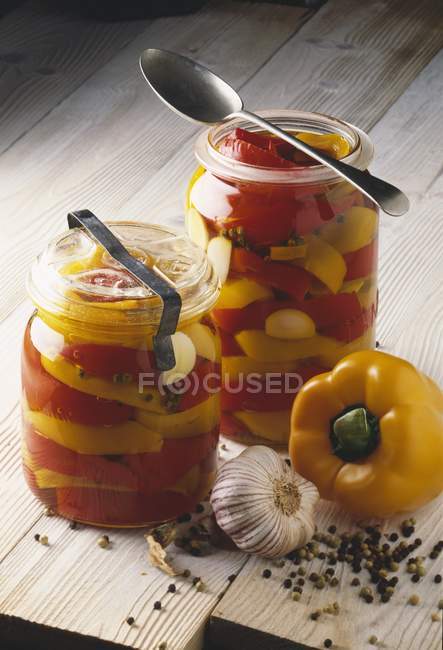 Pots de poivrons jaunes et rouges avec cuillères sur la surface en bois — Photo de stock